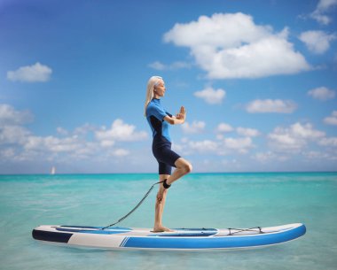 Denizde bir SUP tahtasının üzerinde yoga yapan bir kadının tam boy profil fotoğrafı.
