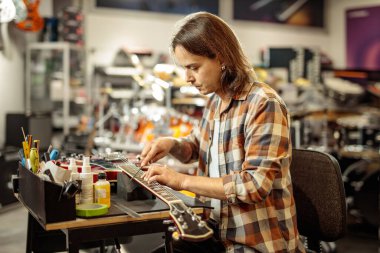 Bir müzik atölyesinde elektro gitar tamir eden bir adam.