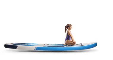 Beyaz arka planda izole edilmiş bir SUP tahtasının üzerinde tek başına oturan küçük kız.