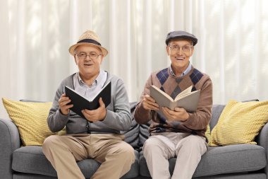 Yaşlı adamlar kanepede oturur ve oturma odasında kitap okurlar.