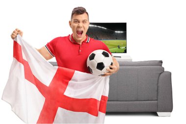 Futbol fanatiği beyaz arka planda izole edilmiş bir kanepe ve televizyon ekranının önünde İngiliz bayrağı tutuyor.