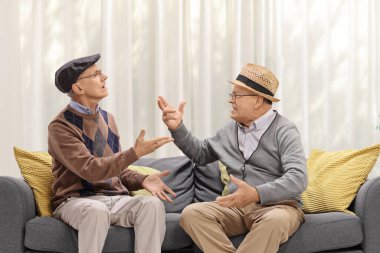 İki yaşlı adam kanepede oturuyor ve tartışıyor.