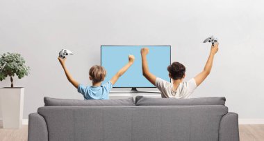 Çocuklar kanepede oturup evde video oyunu oynuyorlar.