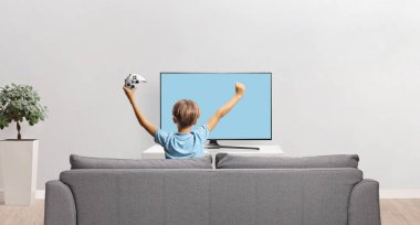 Kanepede oturup beyaz arka planda izole edilmiş bir video oyunu oynayan mutlu bir çocuğun arka plan görüntüsü.