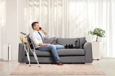 Kırık bacaklı yaralı adamlar evdeki kanepede oturuyor ve akıllı telefon kullanıyorlar.