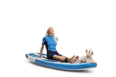 Beyaz arka planda izole bir SUP üzerinde dinlenen ıslak bir teriyer köpeği olan dalış kıyafetli bir kadın.