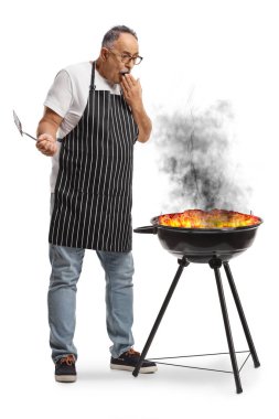 Beyaz arka planda yanan bir bbq 'in yanında duran şok olmuş adam.