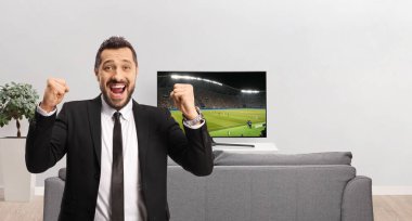 İş adamı futbol maçında TV ekranının önünde mutluluğu işaret ediyor. 