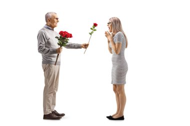 Yaşlı bir adamın beyaz arka planda izole edilmiş genç bir kadına kırmızı gül verirken tam boy profil fotoğrafı.