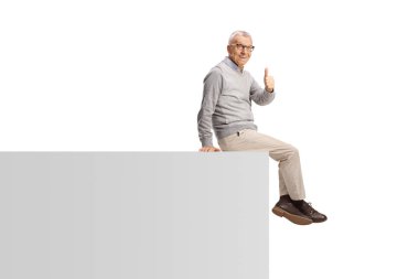 Duvarda oturan yaşlı bir adam ve beyaz arka planda izole edilmiş baş parmakları işaret ediyor.