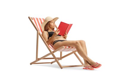 Bikinili genç bir kadın plaj sandalyesinde güneşleniyor ve beyaz arka planda izole edilmiş bir kitap okuyor.