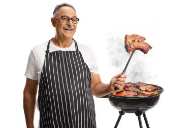 Olgun bir adam barbeküde et pişiriyor ve beyaz arka planda izole edilmiş bir çatalda pişmiş biftek tutuyor.