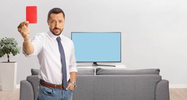 İş adamı evde televizyonun önünde kırmızı kart tutuyor.
