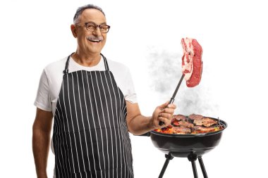 Olgun bir adam barbeküde et pişiriyor ve beyaz arka planda izole edilmiş sığır filetosu tutuyor.