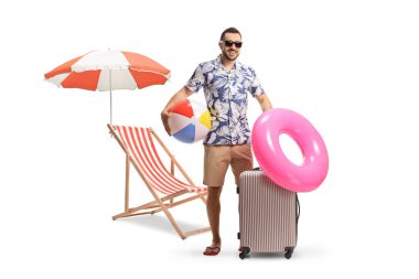 Tatilde bavullu, plaj toplu ve yüzme yüzüklü beyaz arka planda izole edilmiş sandalye ve şemsiyeli bir adam.