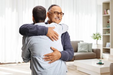 Mutlu adamlar bir oturma odasında birbirlerini kucaklayarak selamlıyorlar.