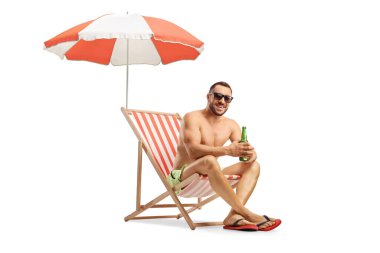 Şemsiyenin altında beyaz arka planda izole edilmiş bir sandalyeye oturmuş bira şişesi tutan adam.