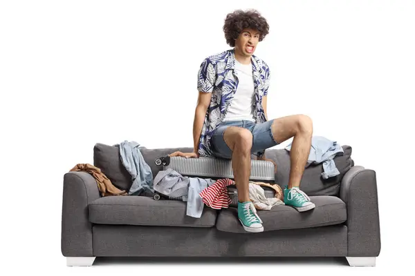 stock image Young man squeezing a suitcase on top of a sofa isolated on white background
