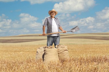 Bir tarlada duran kürek ve çuval beziyle mutlu bir çiftçi.
