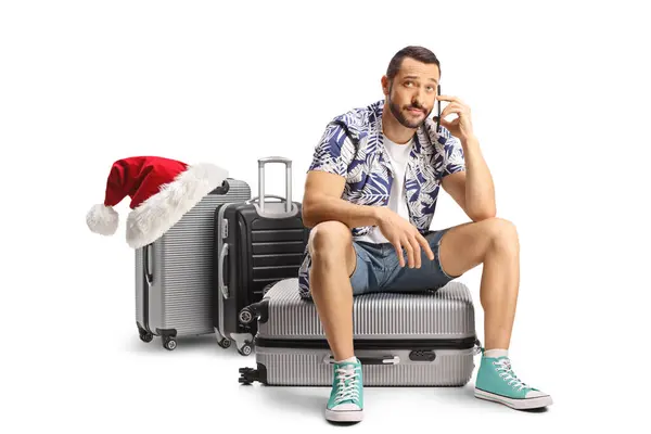 stock image Disappointed male passenger sitting on a suitcase and using a mobile phone, christmas holiday travel concept isolated on white background