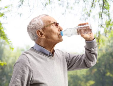 Dışarıda şişeden su içen yaşlı bir adamı yakından çek.
