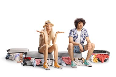 Bavulların üzerinde oturan ve beyaz arka planda izole edilmiş bekleyen genç çift.