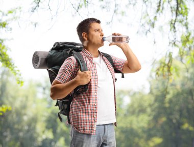 Sırt çantalı bir erkek turist parktaki bir şişeden su içiyor.