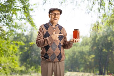 Elderly man holding a jar of honey in nature and pointing clipart