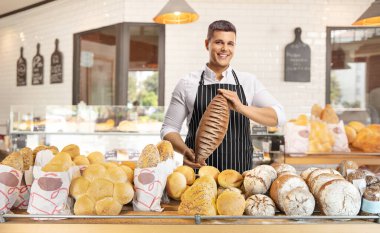 Önlük takan ve fırının içinde bir somun kahverengi ekmek tutan gülümseyen genç fırıncı.