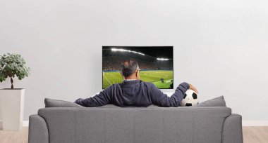 Erkek futbol eğlencesi evdeki TV karşısında bir kanepede oturuyor.