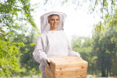 Young female bee keeper in a uniform holding a wooden box  clipart