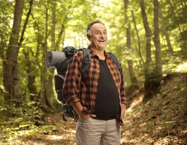 Ormanda gülümseyen sırt çantalı olgun bir yürüyüşçü.