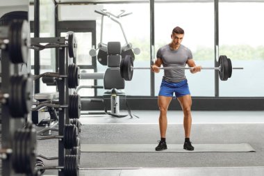 Spor kıyafetli, spor salonunda ağırlık kaldıran güçlü bir gencin tam boy portresi.