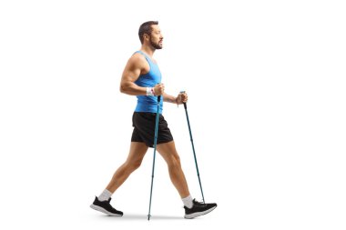 Beyaz arka planda izole edilmiş yürüyüş direkleriyle yürüyen genç bir adamın tam boy profil çekimi.