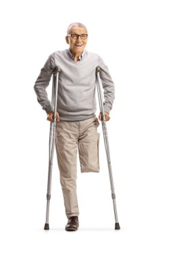 Bacağı kesilmiş yaşlı bir adam beyaz arka planda izole edilmiş koltuk değnekleriyle ayakta duruyor.
