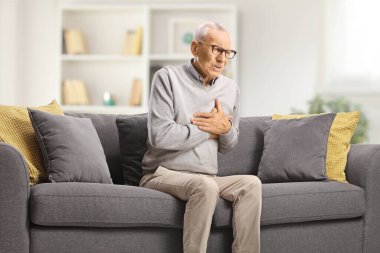 Oturma odasındaki bir kanepede kalp krizi geçiren yaşlı bir adam.