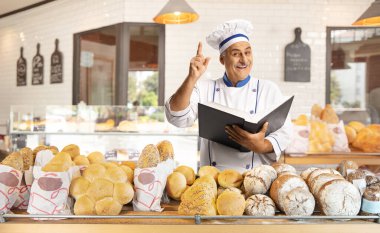 Olgun bir aşçı fırının içinde yemek kitabı tutuyor.