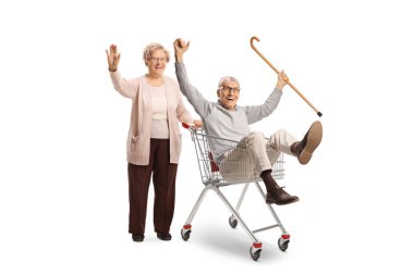 Yaşlı bir adamla birlikte yaşlı komik bir kadın beyaz arka planda izole bir alışveriş arabasında oturuyor.