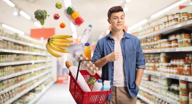 Marketteki genç adam elinde sepetine düşen ürünlerle bir alışveriş sepeti tutuyor. 