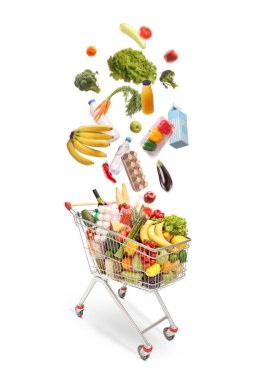 Farklı gıda ürünleri beyaz arka planda izole edilmiş bir alışveriş arabasına düşüyor.