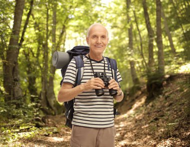Yetişkin bir erkek yürüyüşçü ormanda dürbün tutuyor.