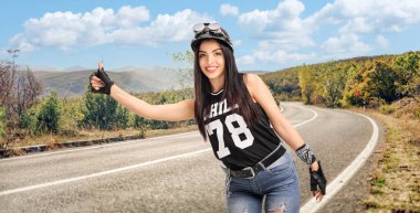 Young female biker with helmet and goggles hitchhiking on a road clipart