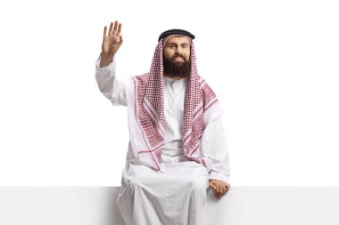 Suudi Arabistan 'lı adam boş bir panelde oturuyor ve beyaz arka planda izole bir şekilde el sallıyor.
