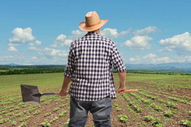 Bir çiftçinin tarlaya baktığı ve elinde kürek tuttuğu arka plan görüntüsü.