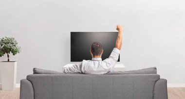 Evdeki kanepede oturmuş televizyon seyreden bir adam.