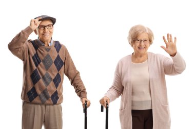 Yaşlı bir adam ve kadın ellerinde bastonlarıyla ayakta duruyor ve beyaz arka planda izole bir şekilde el sallıyorlar.