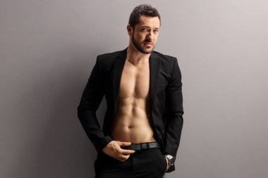 Siyah takım elbiseli, gri duvarda poz veren gömleksiz bir erkek model. 