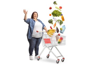 Mutlu kadın el sallıyor, elinde alışveriş arabasıyla dikiliyor ve beyaz arka planda izole bir şekilde alışveriş yapıyor.