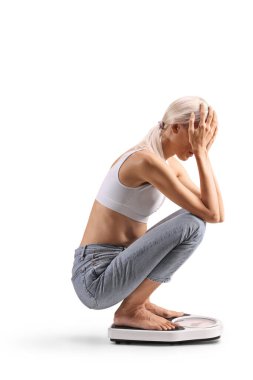 Beyaz arka planda izole edilmiş ağırlık ölçeğinde duran endişeli genç bir kadın.