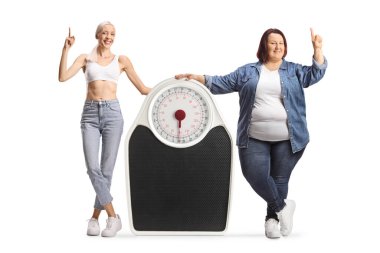 Zayıf ve kilolu bir kadın bir ağırlık terazisinin yanında duruyor ve beyaz arka planda izole bir şekilde duruyor.